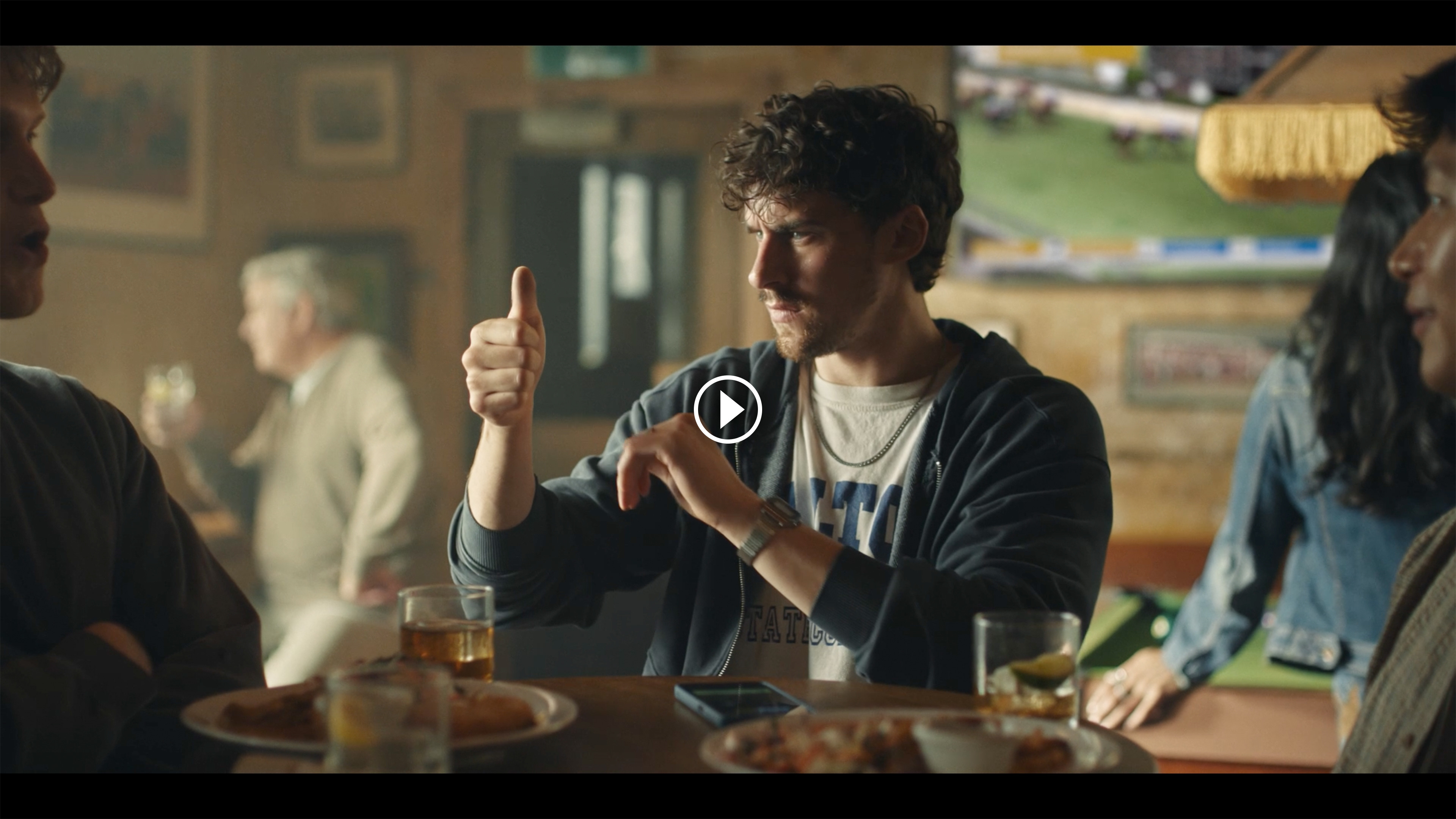 A young male in a pub is looking at this thumb at eye level with a look of confusion